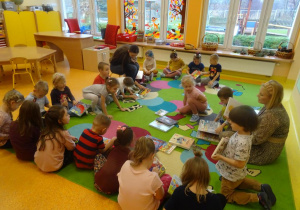 Dzieci siedzą na dywanie i oglądają książki.